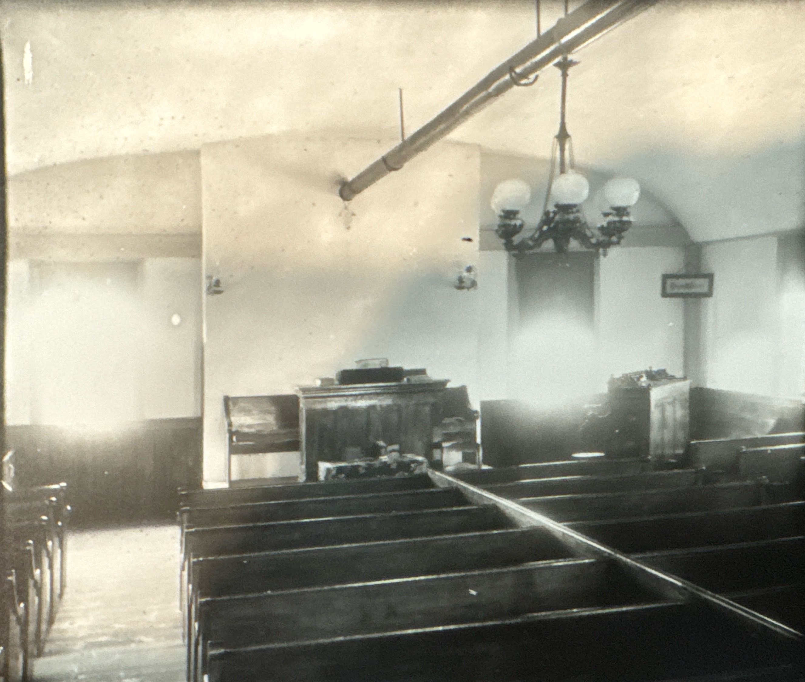 Interior of Harmony Hall during its chapel years, wooden pews, a pulpit, and original hanging oil lamps
